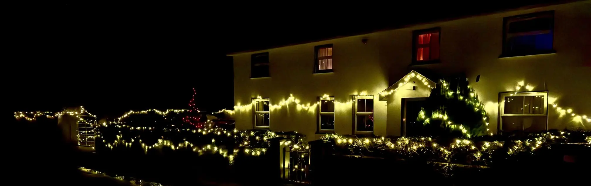 A farm house adorned with festive yellow string lights is illuminated at night.
