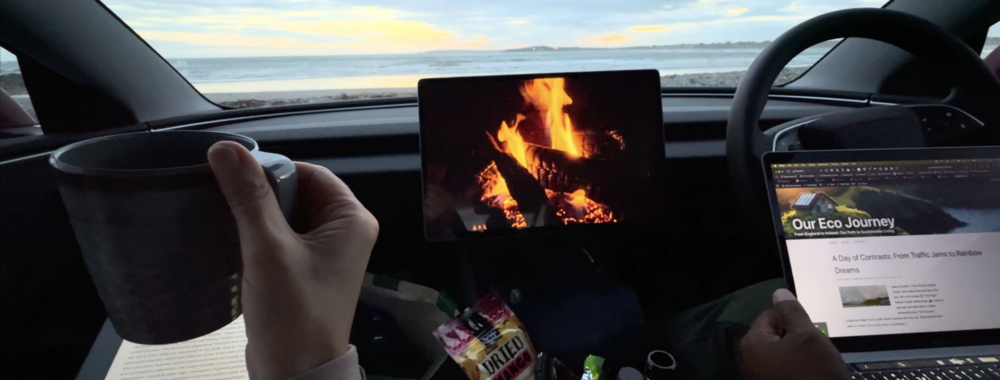 Helen holding a mug in a car by the beach, with a tablet showing a fireplace and a laptop displaying an article titled "Our Eco-Journey.