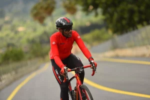 Kenn in red and black gear rides a bike on a winding road lined with trees.