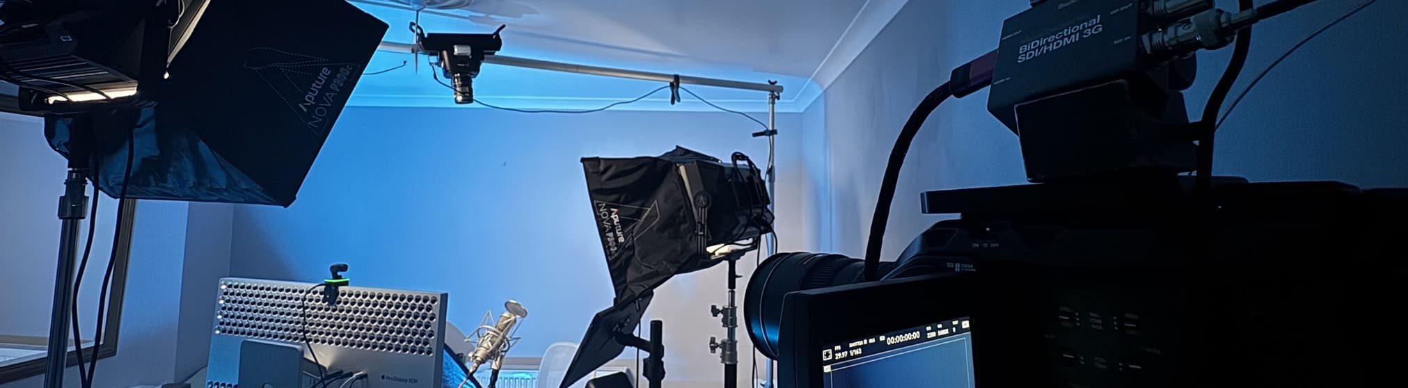 Kenn's office set up as a video studio with professional lighting, cameras, and a microphone against a blue-lit wall.
