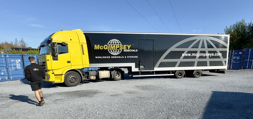 A large yellow and black McGimpsey Removals truck is parked on gravel, with a man in dark clothing walking nearby.