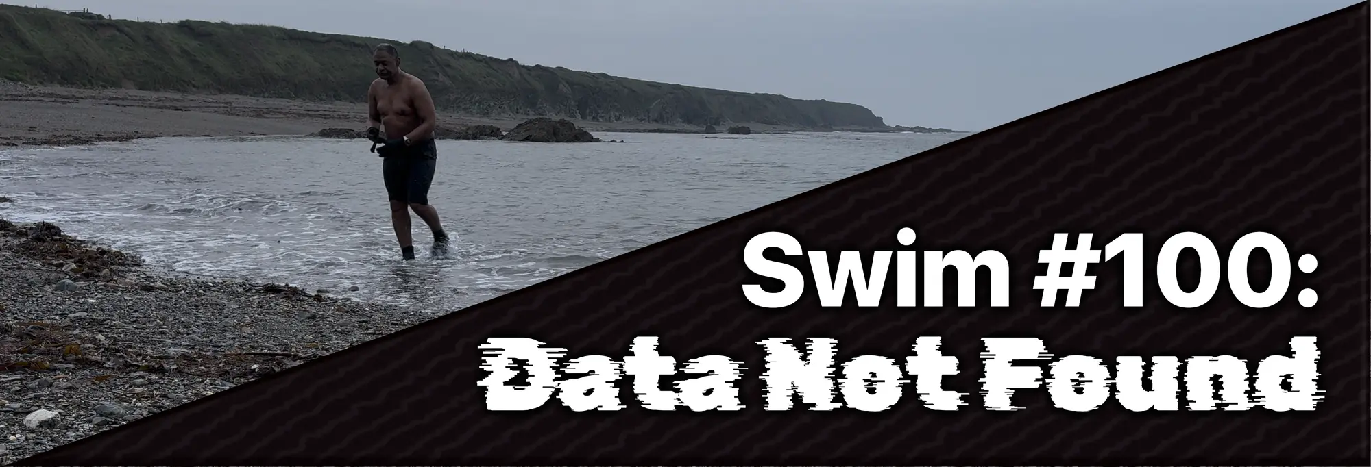 Kenn walks out of the sea onto a rocky beach under an overcast sky; text overlay reads "Swim #100: Data Not Found.