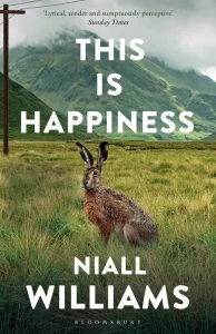 Book cover for "This Is Happiness" by Niall Williams, featuring a hare in a grassy field with hills in the background.