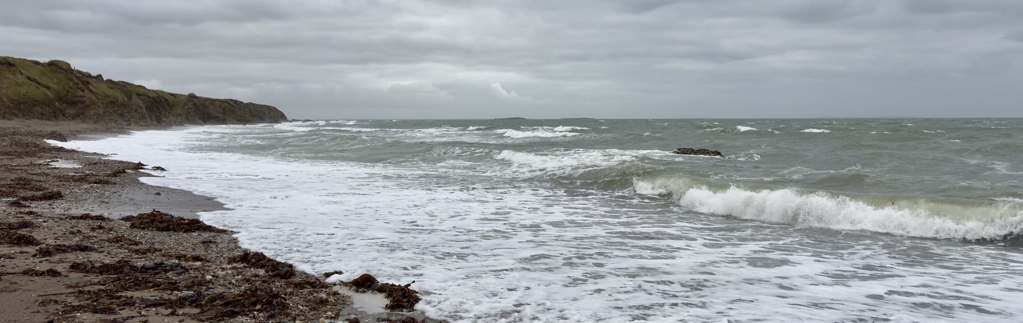 Cloudy sky over a rocky beach with waves crashing against the shore.