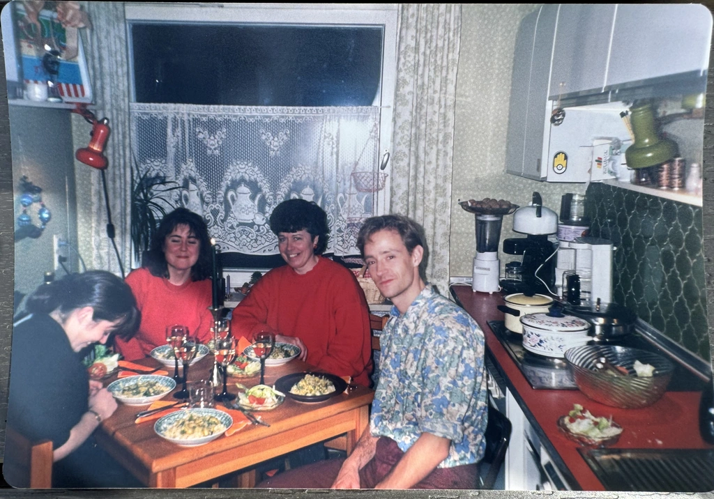 Sabine, my wife Helen, her Mum Anne and Peter sitting around a small kitchen table set with plates of food and glasses in a cozy, cluttered kitchen. One person is laughing with their head down.